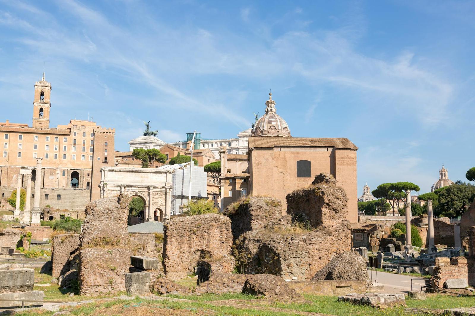 Ancient ruined walls beside a domed church tower under a bright sky