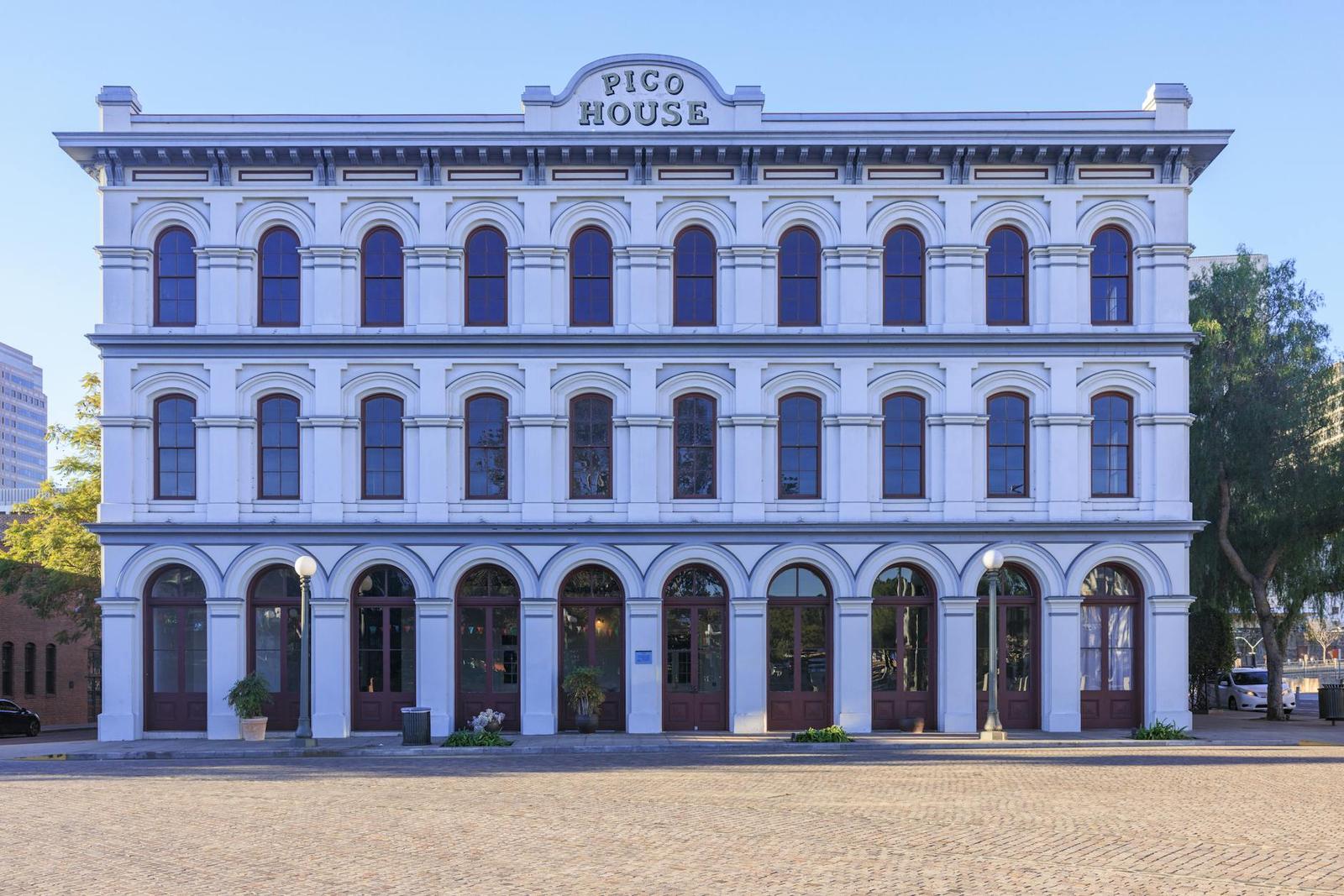 A white arched historic building with a rooftop sign above a brick plaza