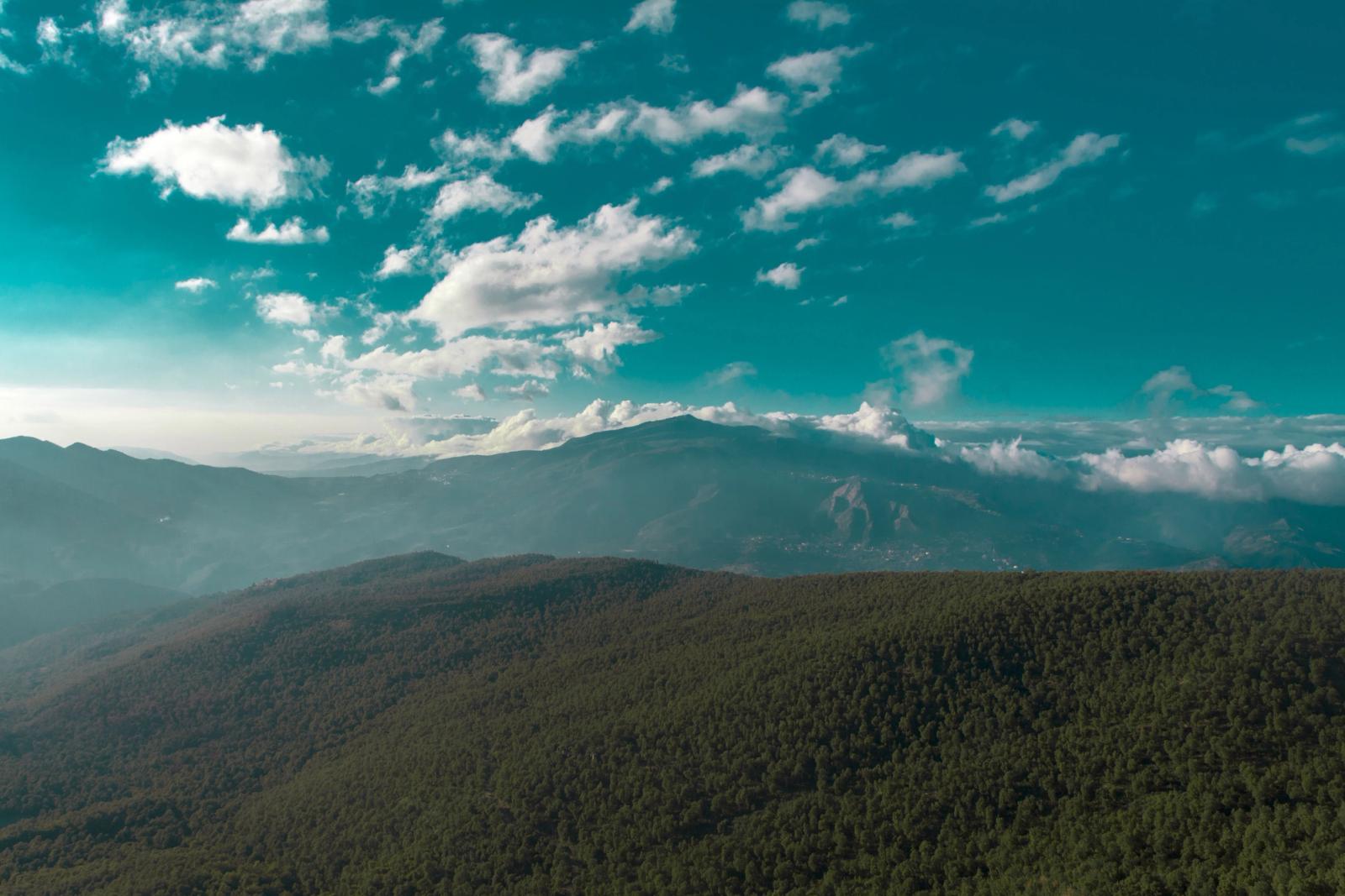 Breathtaking aerial view of lush green mountains beneath a blue sky with scattered clouds