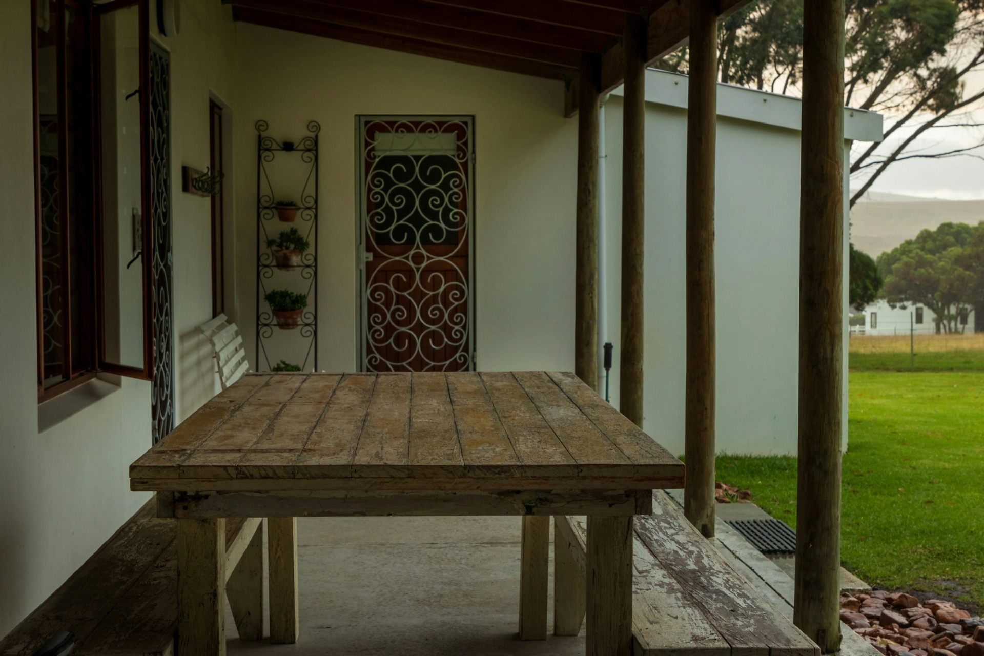 A covered stone patio with a wooden table beside an ornate iron door