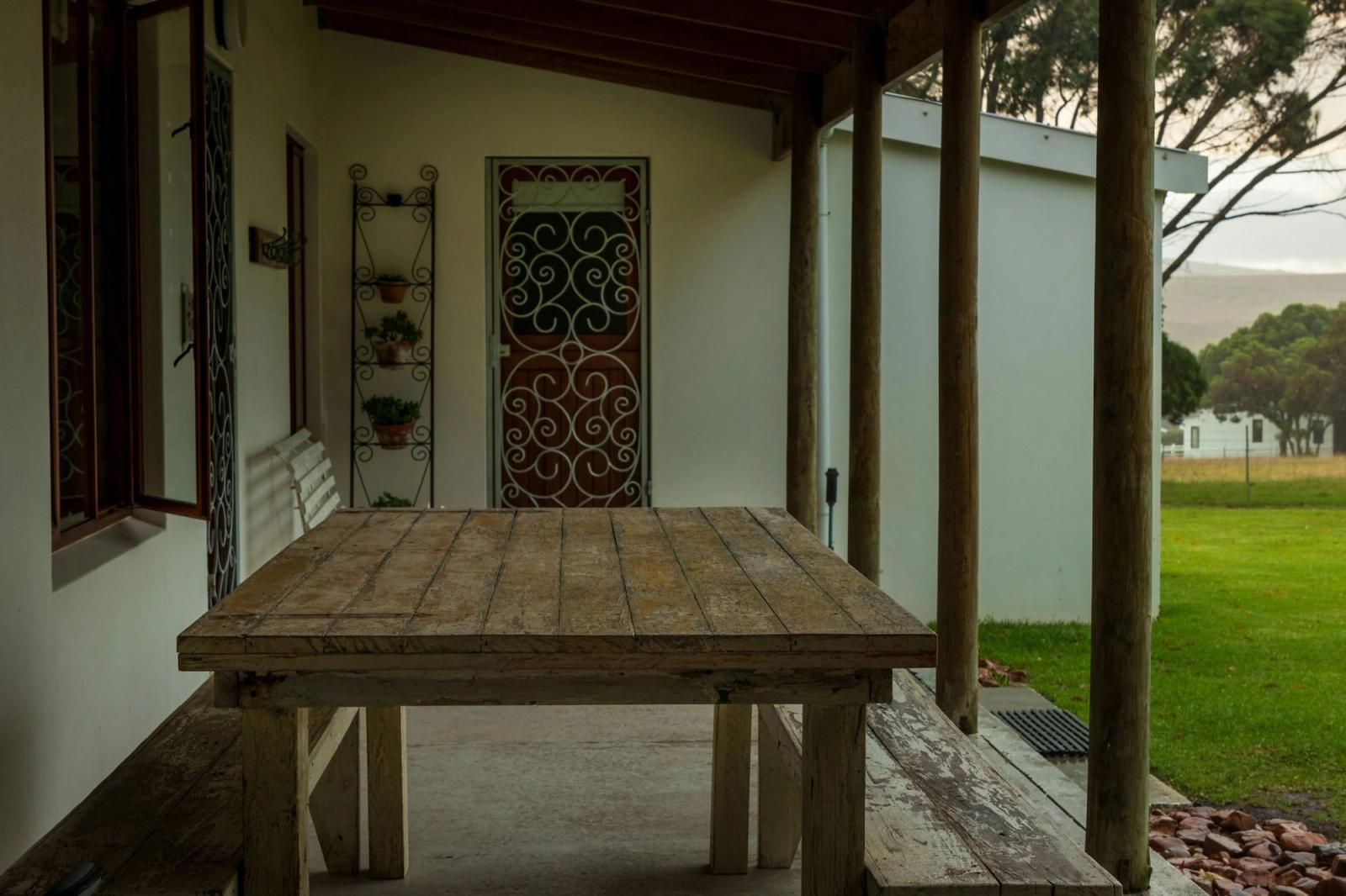 A covered stone patio with a wooden table beside an ornate iron door
