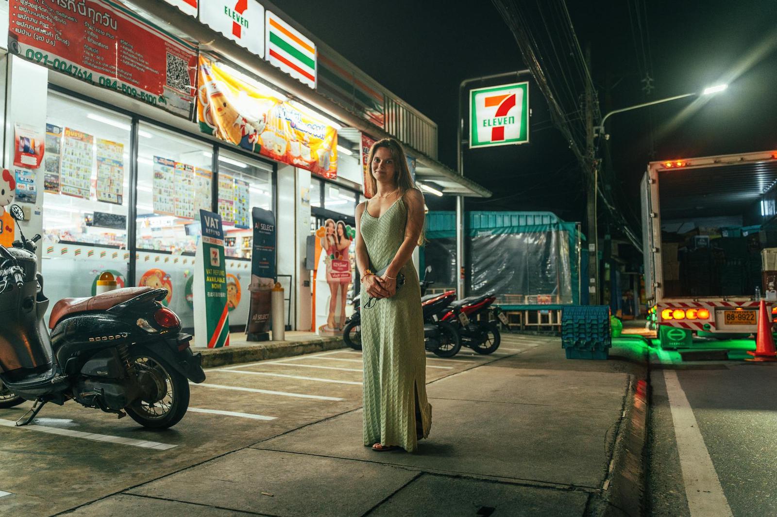 A woman in an evening dress standing outside a convenience store at night