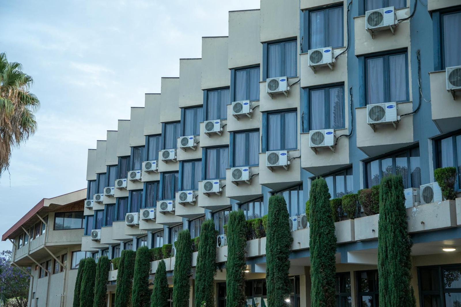 A stepped hotel facade lined with balcony air conditioning units and cypress trees