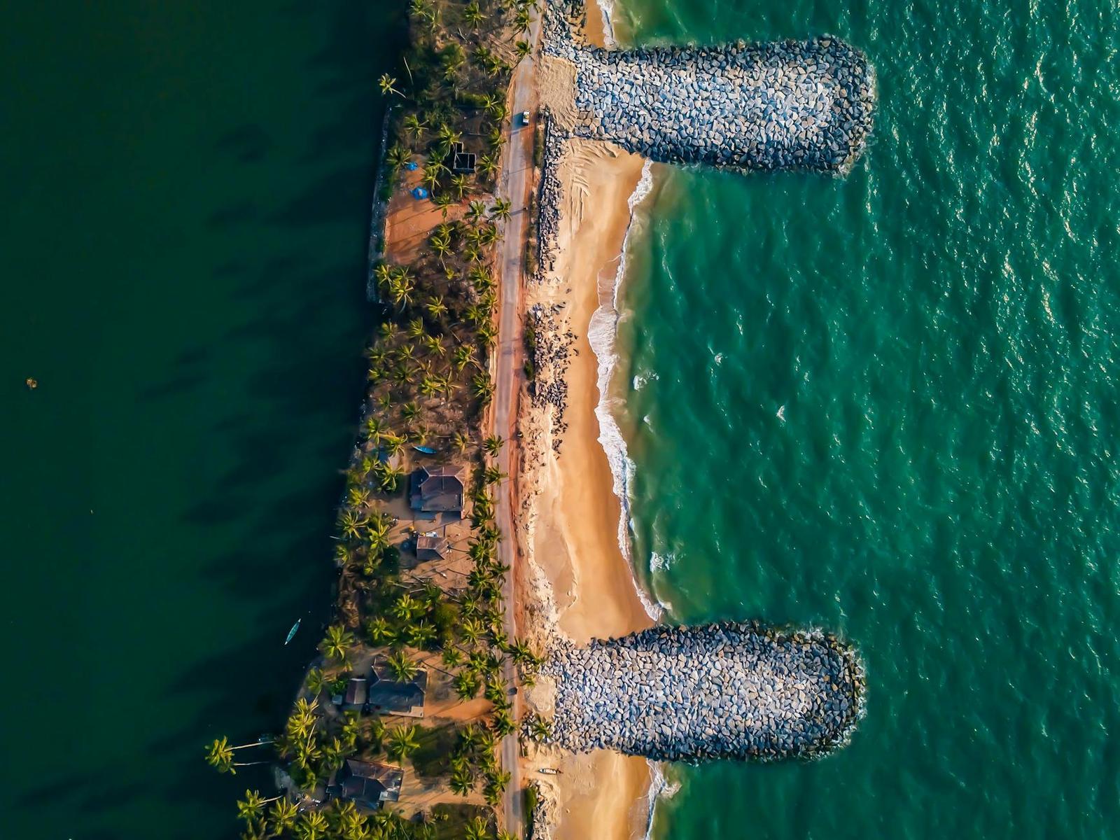 Aerial view of a palm-lined shore between two stone breakwaters in green water