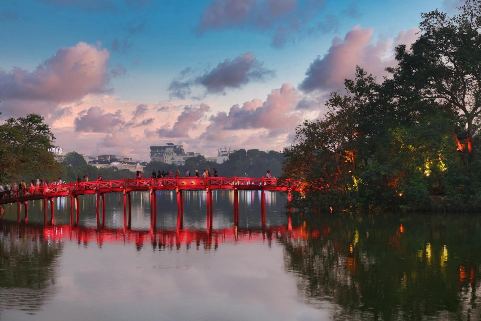 Red lacquered bridge crossing a lake toward a tree-lined shore at dusk