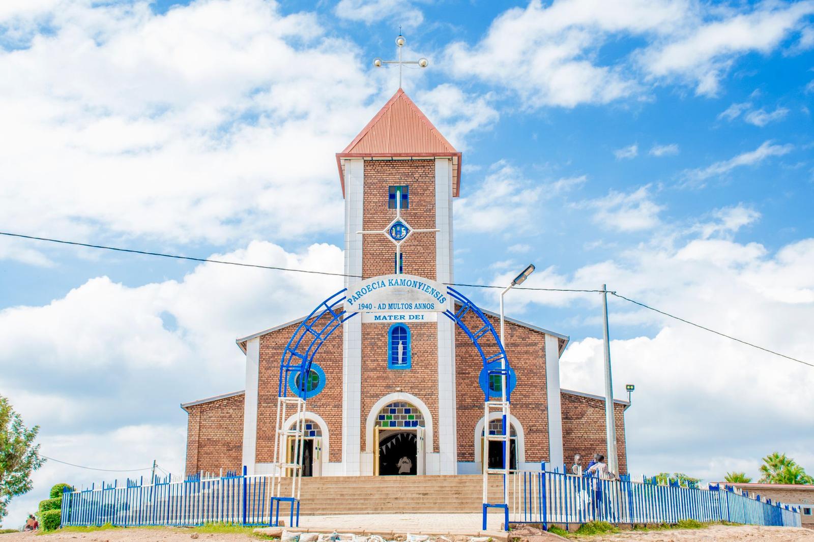 A picturesque Catholic church with a distinctive red roof and blue accents under a vibrant sky