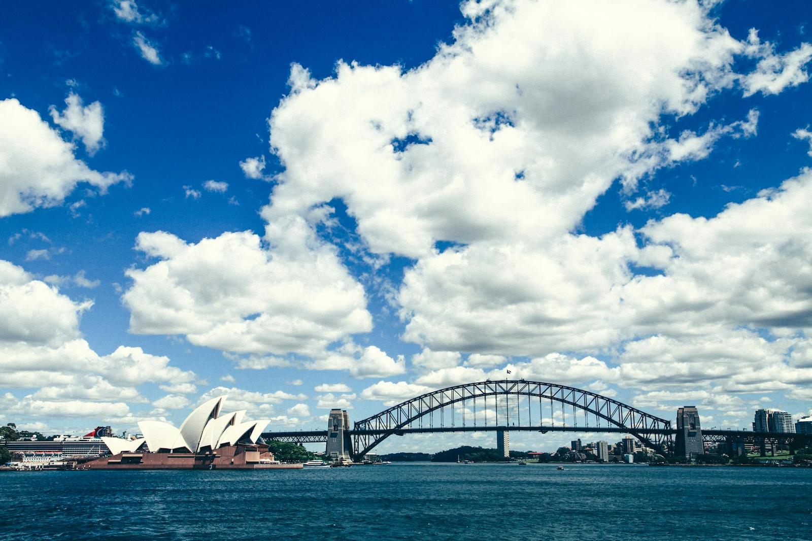 A stunning view of the Sydney Harbour Bridge and Opera House with a bright blue sky and white clouds