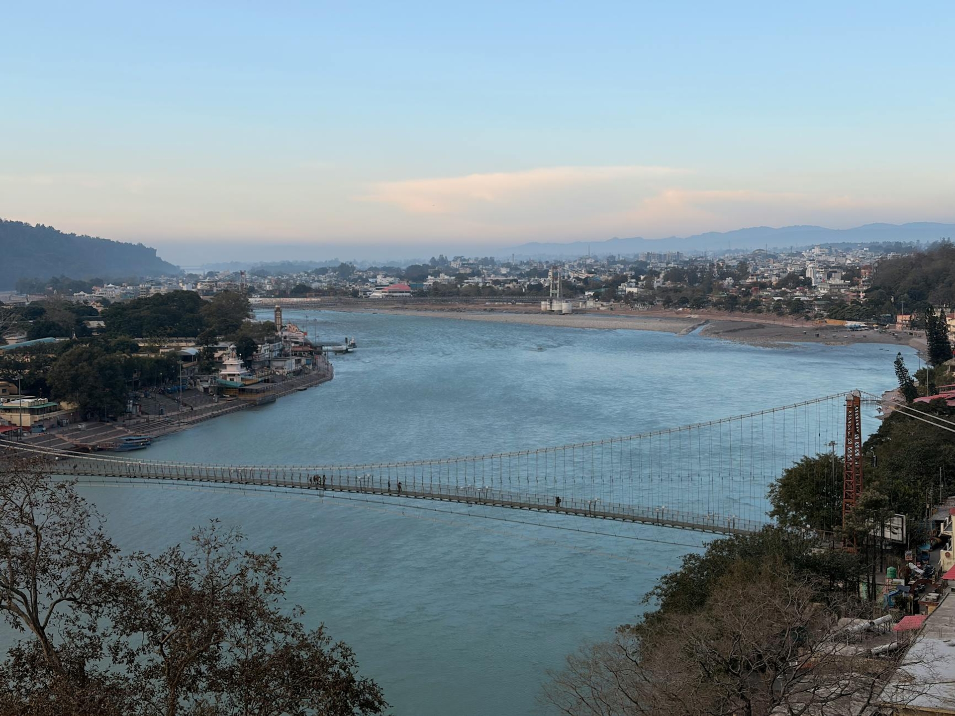 A wide river bend crossed by a suspension footbridge below a hillside town