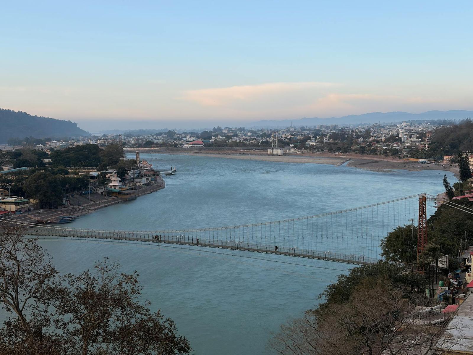 A wide river bend crossed by a suspension footbridge below a hillside town