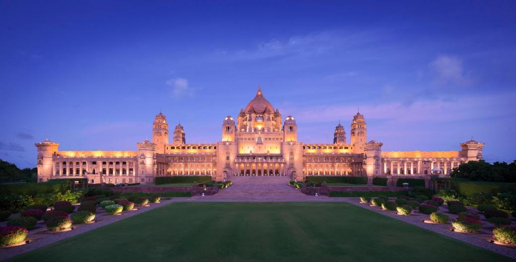 Umaid Bhawan Palace lit at twilight, golden sandstone facade over manicured lawns