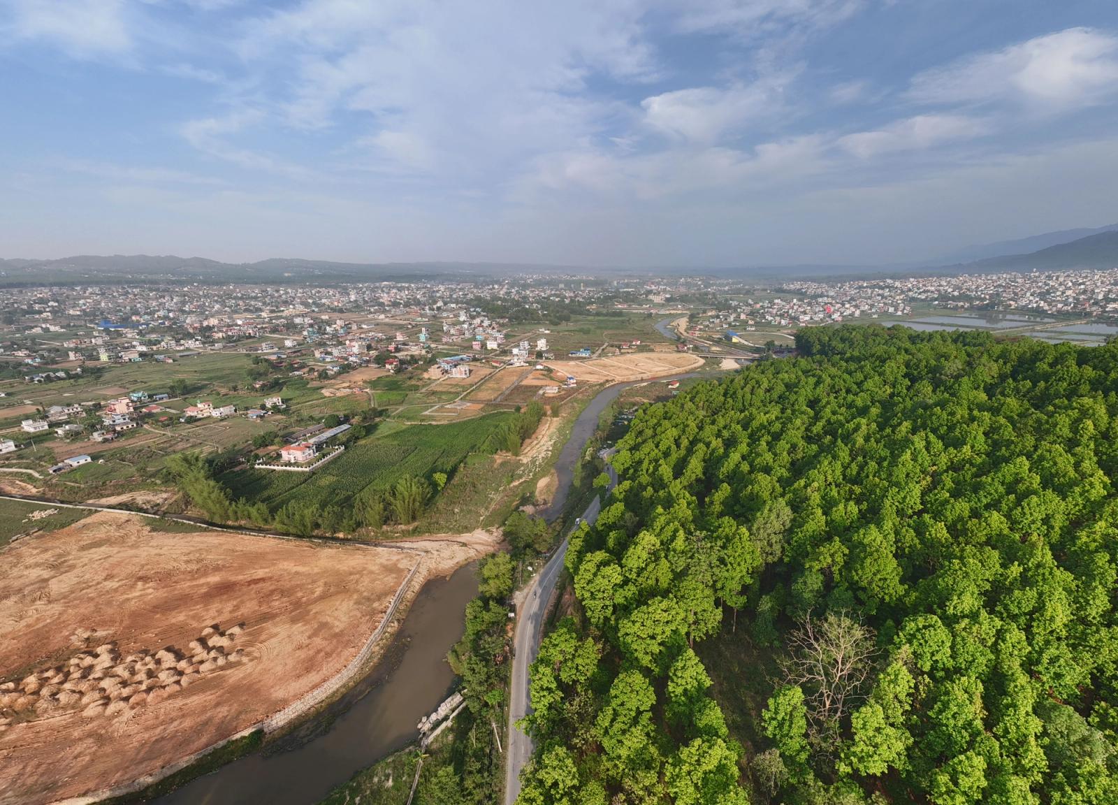 A scenic aerial view showcasing lush green forests alongside an expanding city under the bright sky