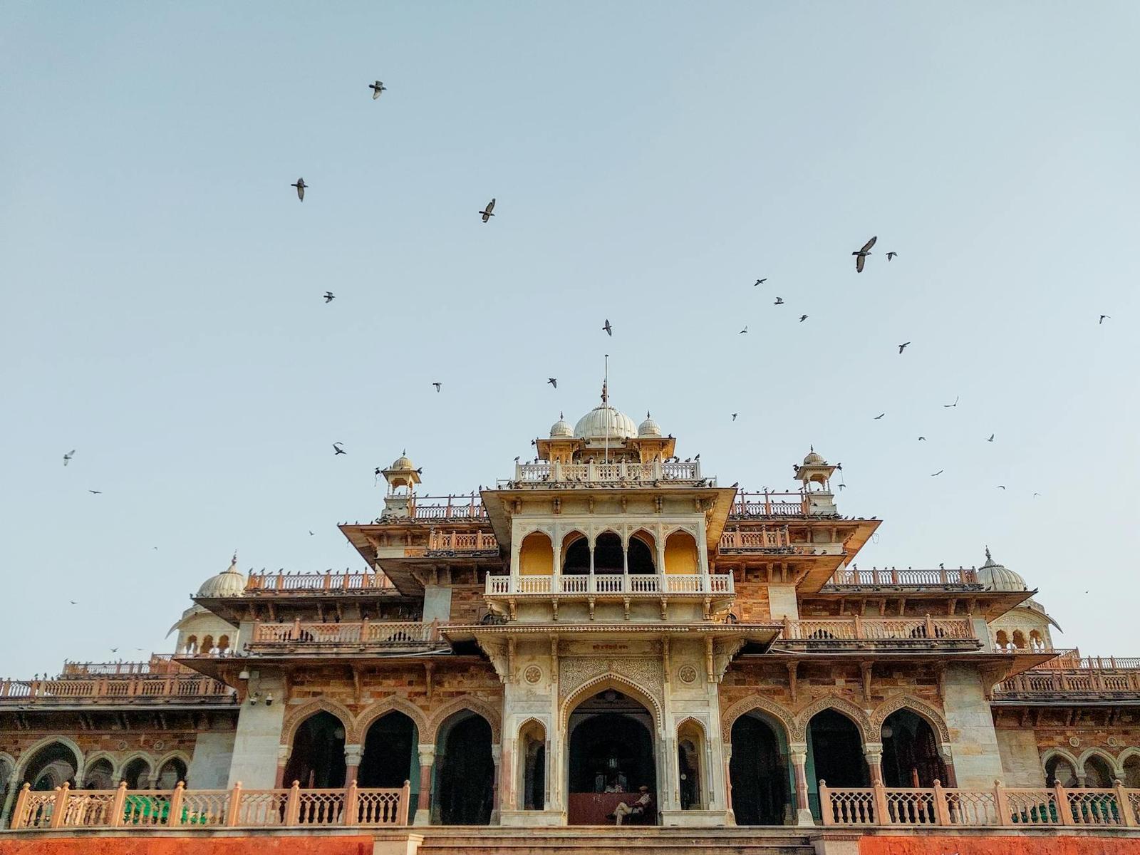 A domed sandstone building with birds circling in the evening sky