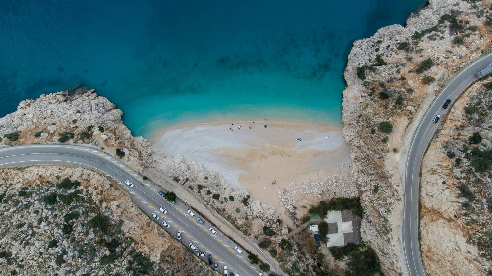 Aerial view of a winding coastal road curving around a hidden cove beach