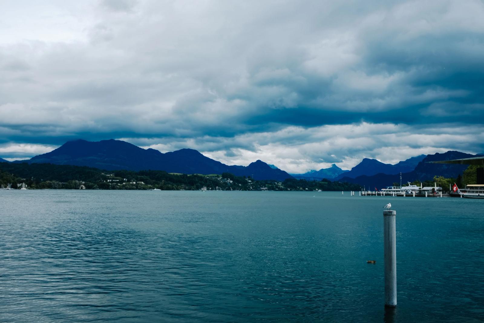 A serene coastal view with mountains and overcast clouds reflecting on the calm sea