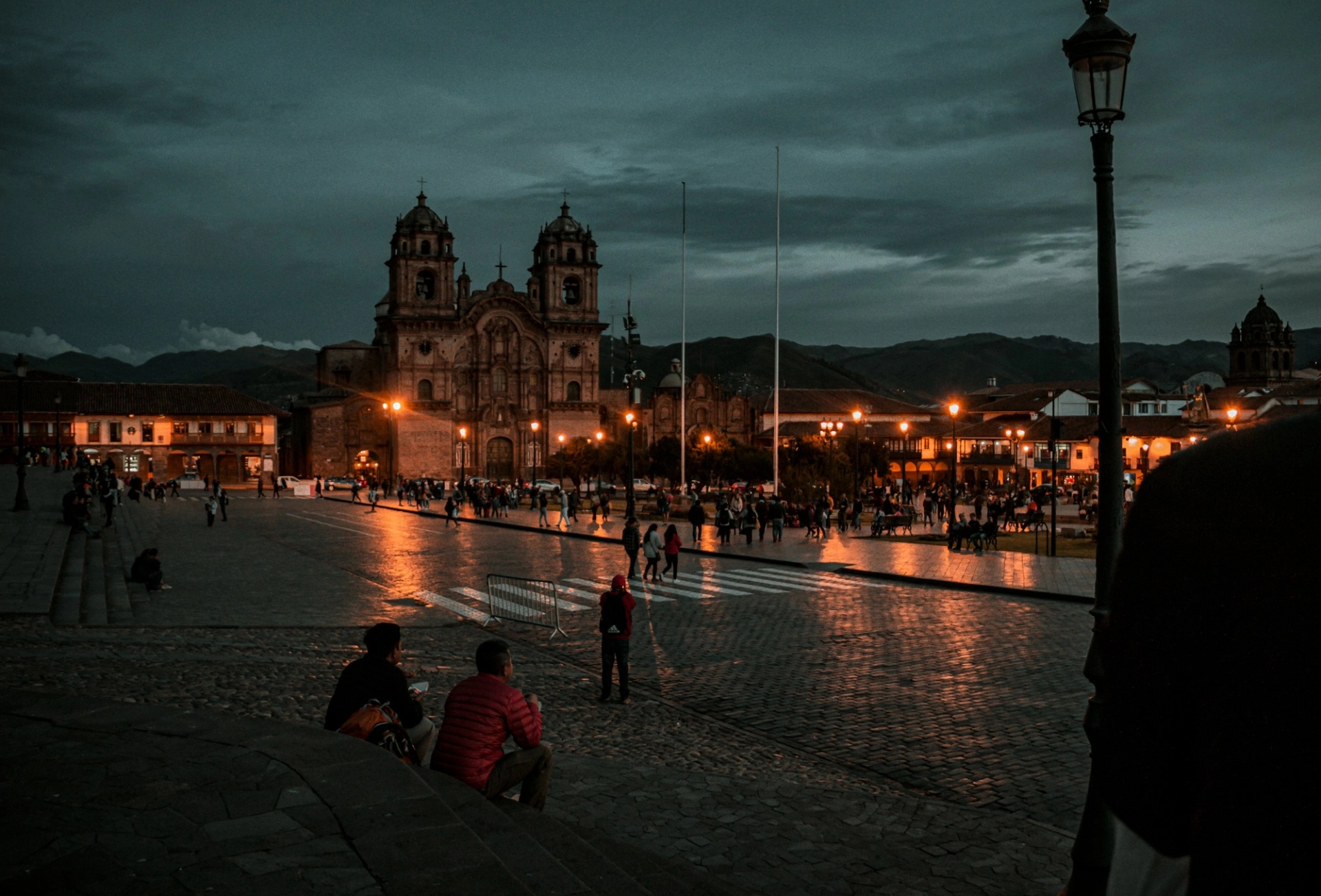 A floodlit cathedral overlooking a plaza at dusk with people gathered below