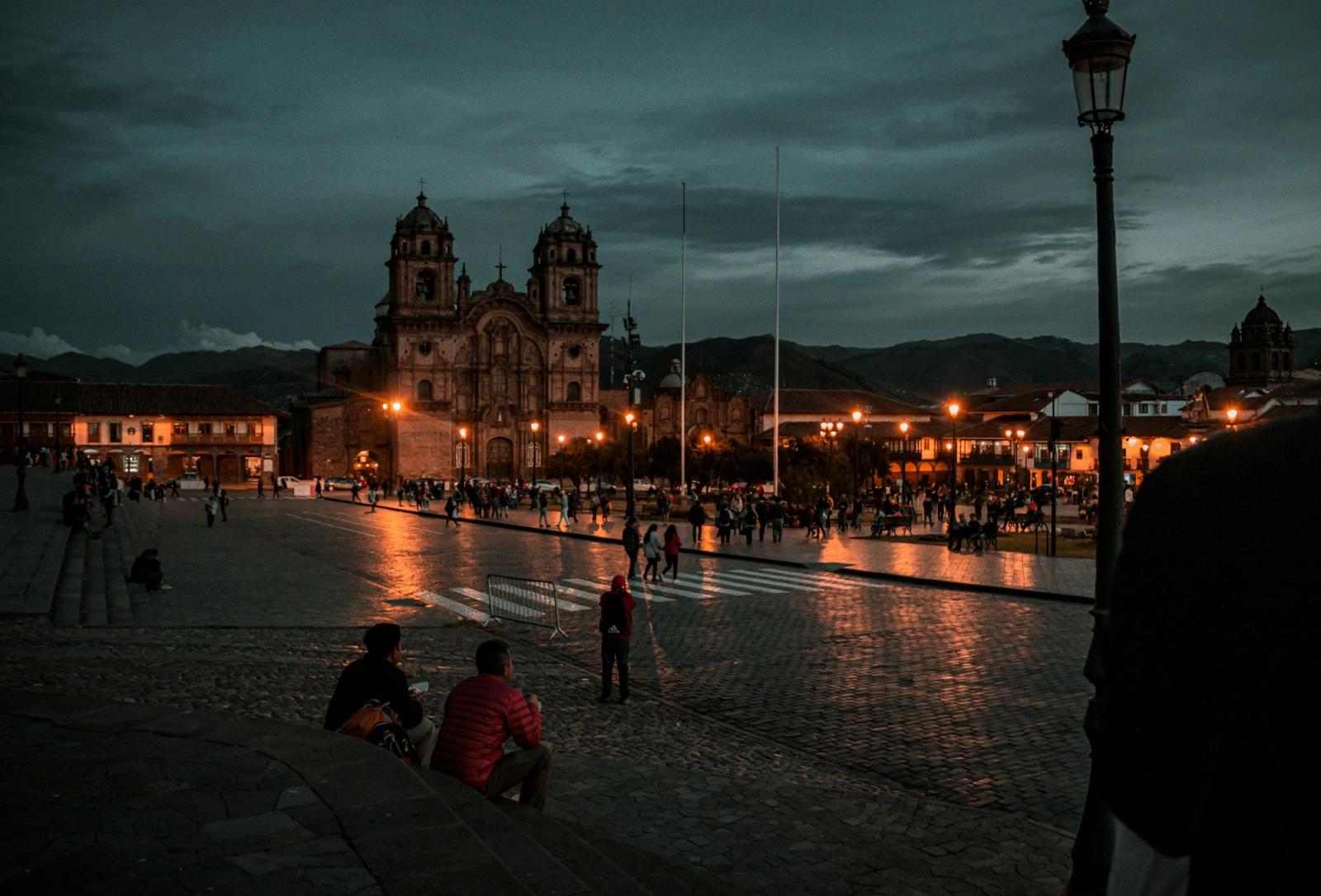 A floodlit cathedral overlooking a plaza at dusk with people gathered below