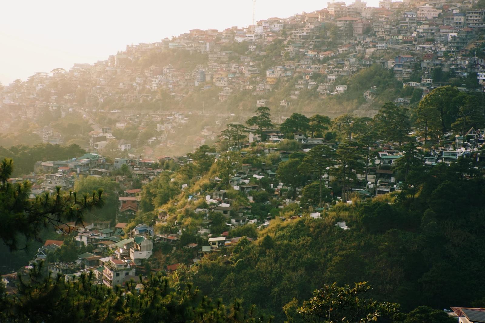 A stunning view of the hillside residential area in Shimla, India, surrounded by lush trees and summer lighting