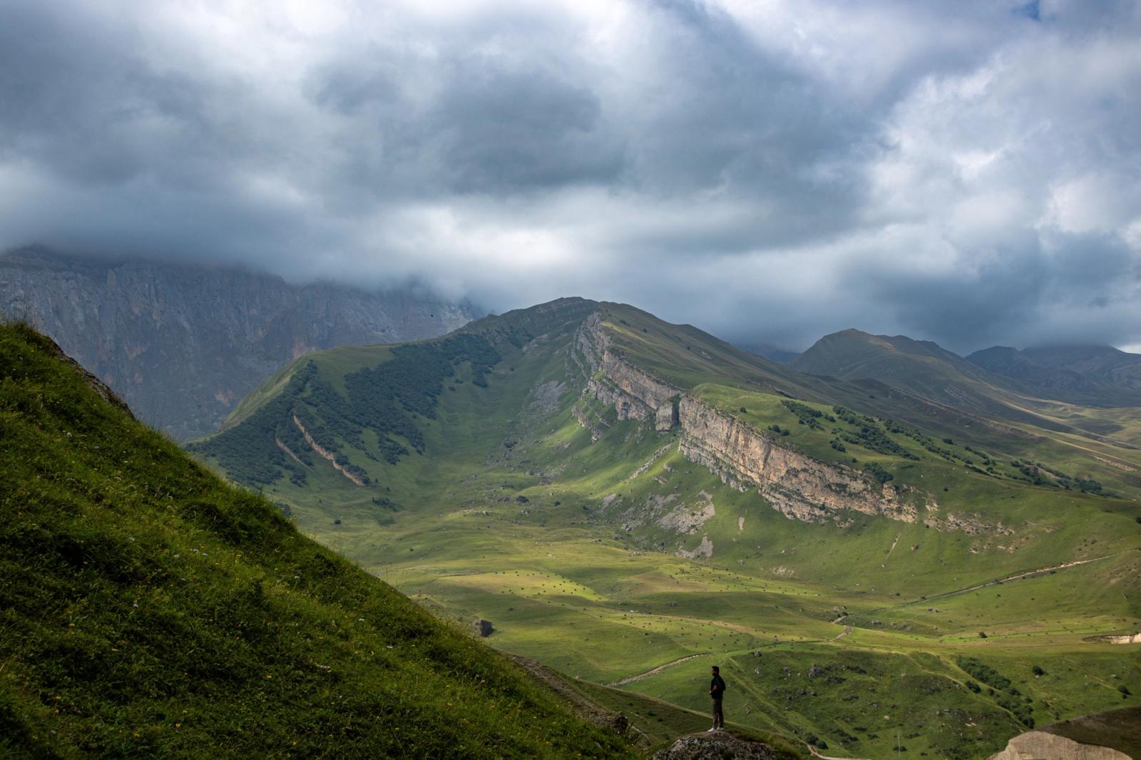 A distant hiker silhouetted on a green ridge under a stormy sky