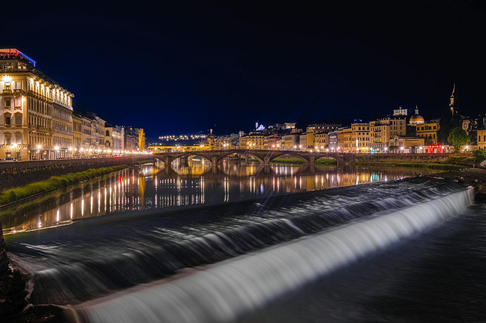 Arched stone bridge over a river with a lit weir at night