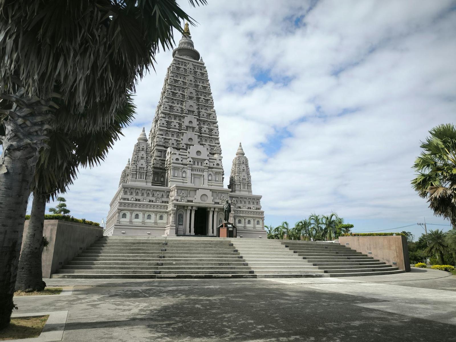 A white stepped temple tower with a palm tree beside a wide stone plaza