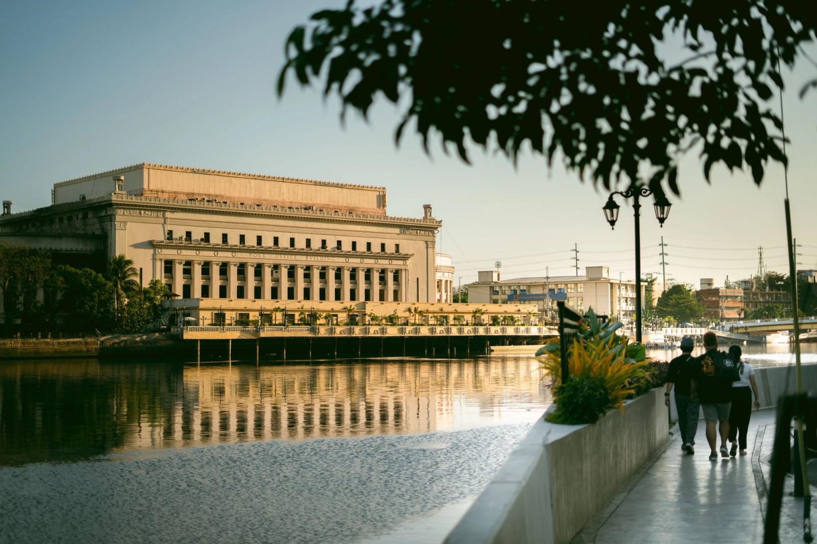 A serene view of the Manila Central Post Office building along the riverbank, capturing urban beauty at daytime