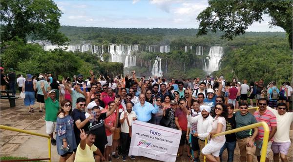 A large group posing with a banner at a scenic waterfall location.