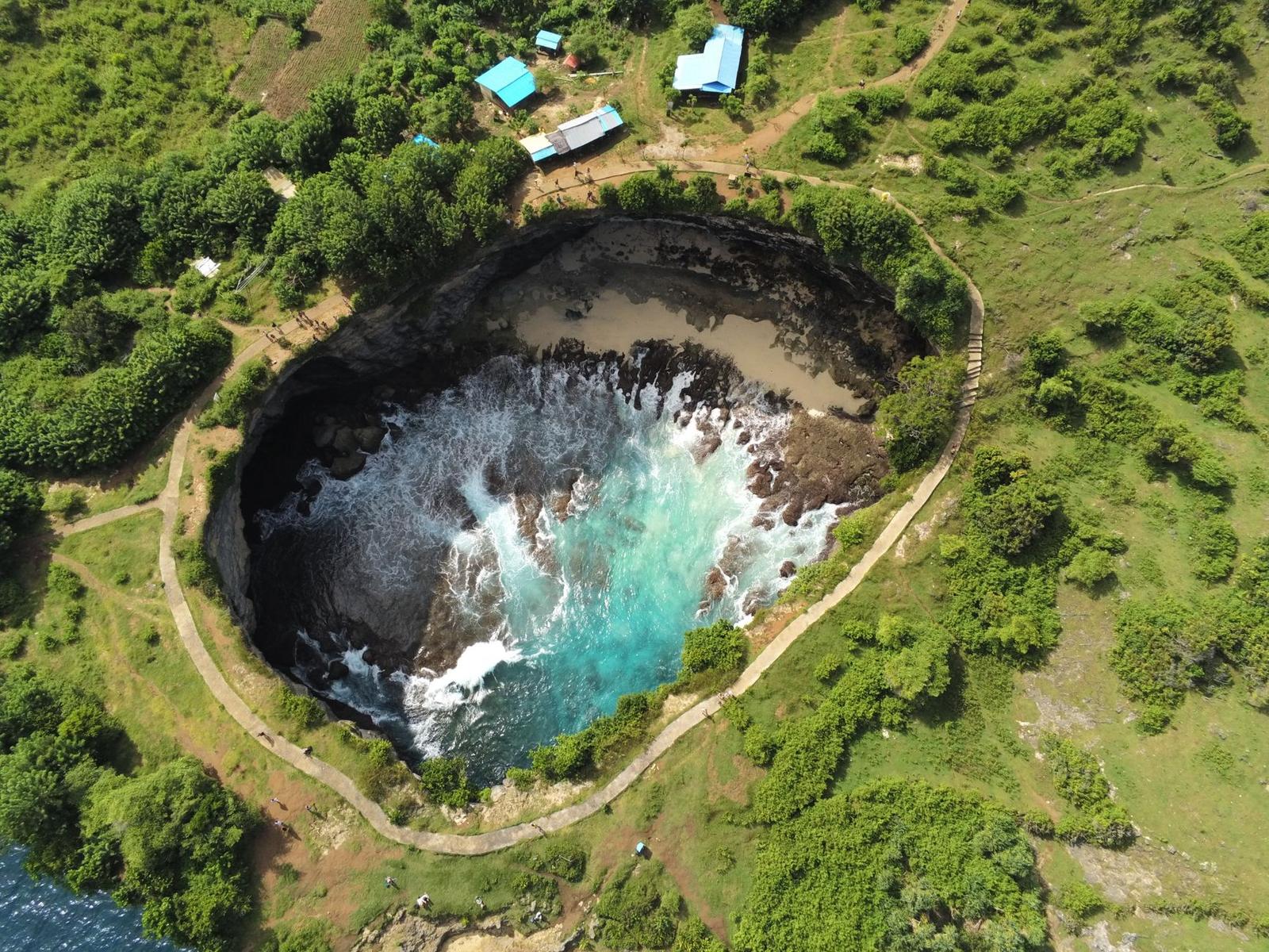 Aerial view of a circular turquoise lagoon carved into a coastal cliff