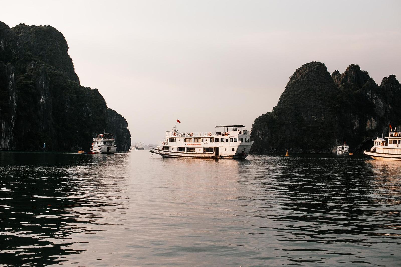 White tour boats moving between towering limestone karsts on calm water