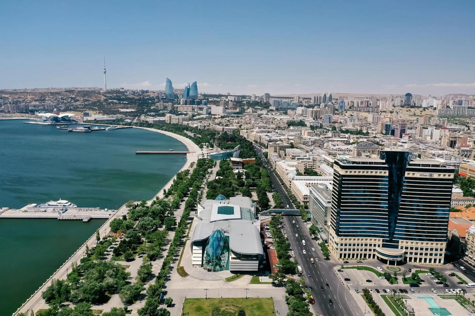 Aerial view of a curved glass tower and museum along a waterfront promenade