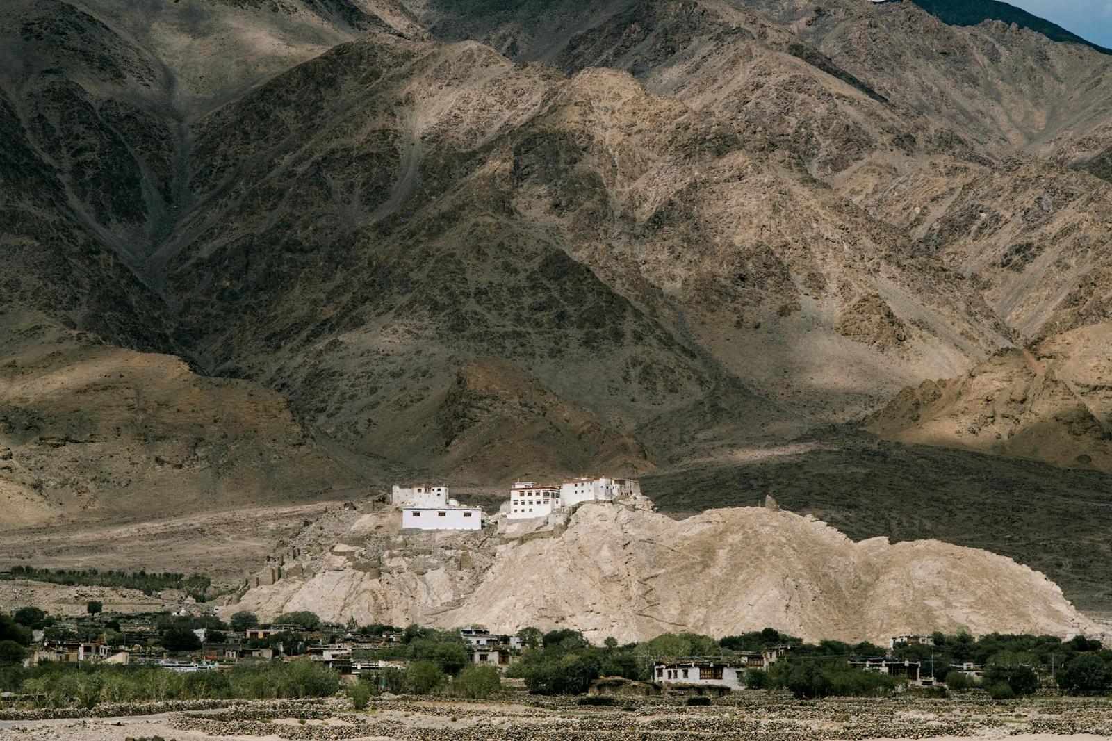 A whitewashed monastery on a hillside surrounded by rugged mountains
