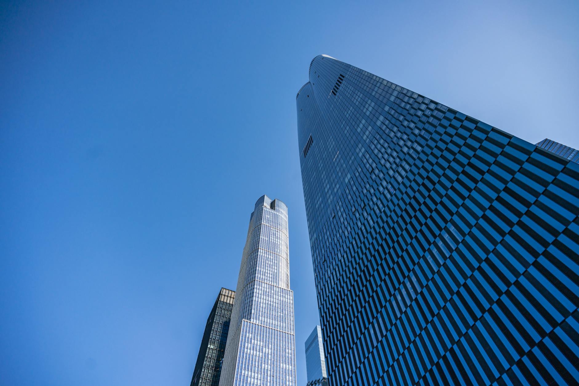 Looking up at two glass skyscrapers converging against a clear blue sky
