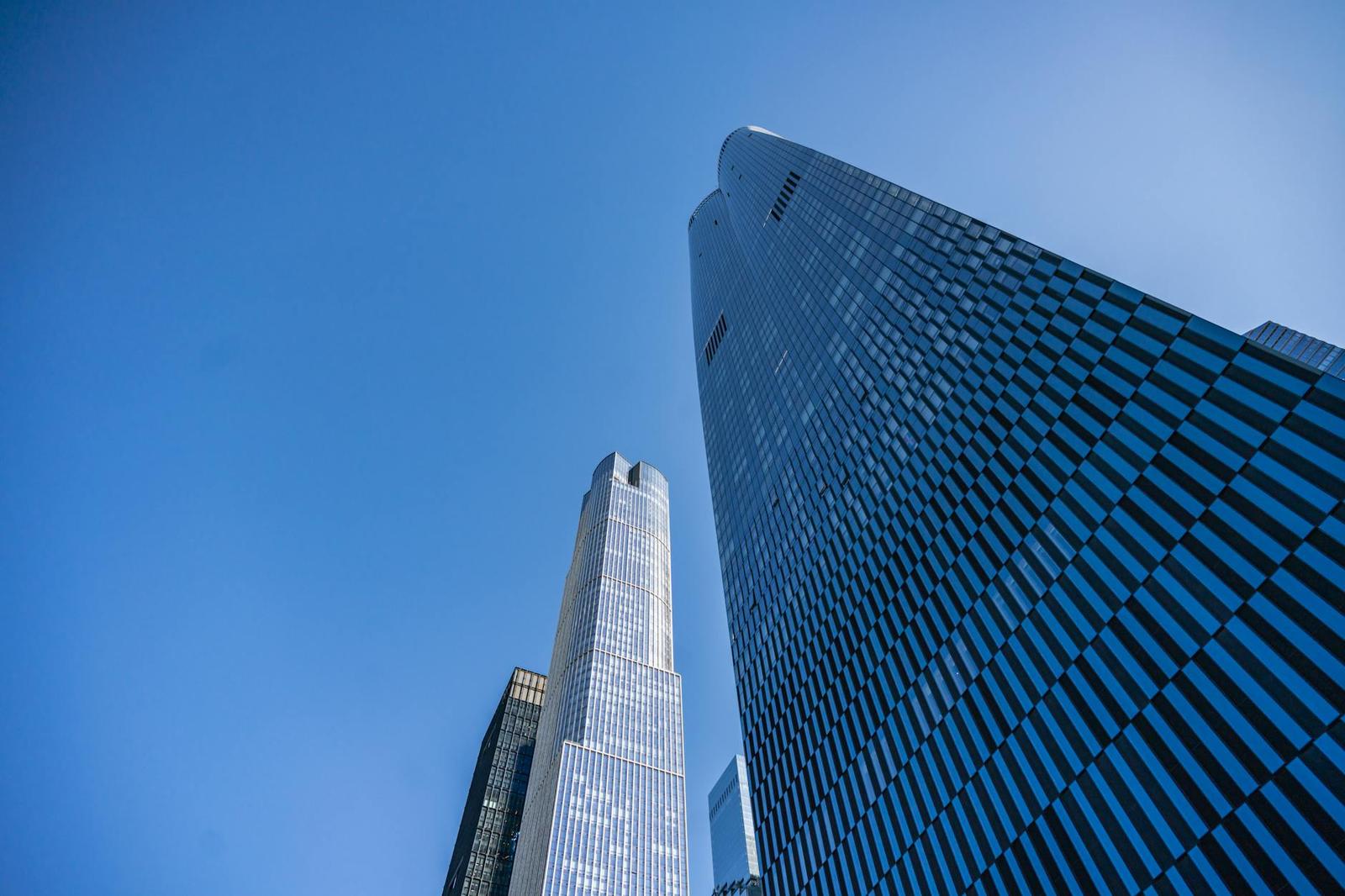 Looking up at two glass skyscrapers converging against a clear blue sky