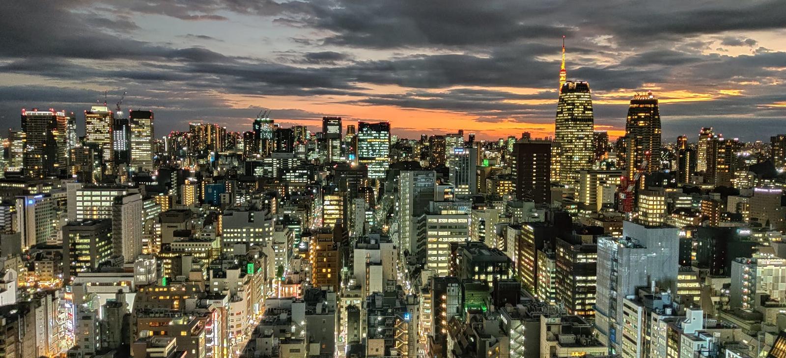 A wide city skyline glowing at dusk with a tall lit spire on the right
