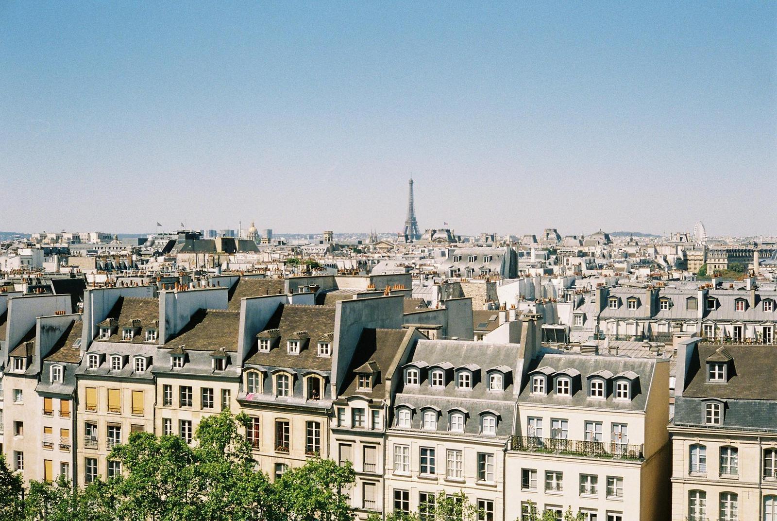 A scenic aerial view of Paris rooftops with the Eiffel Tower in the background under a clear blue sky