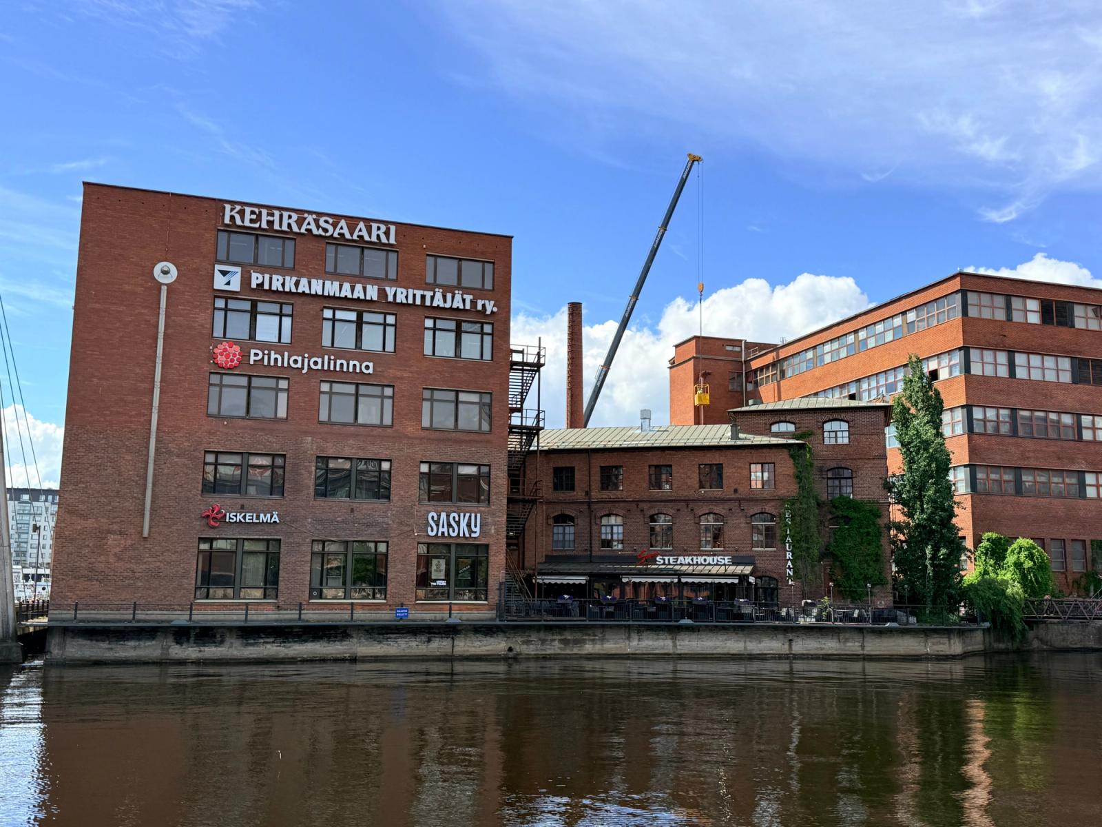 Scenic view of Kehräsaari red brick buildings along the river in Tampere, Finland, on a sunny day