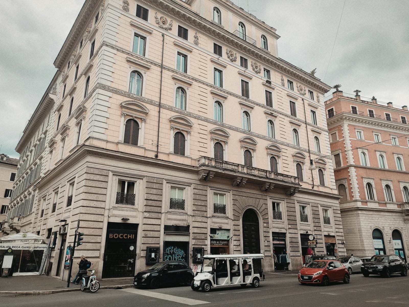 Cream stone corner building at a city intersection with cars and pedestrians below