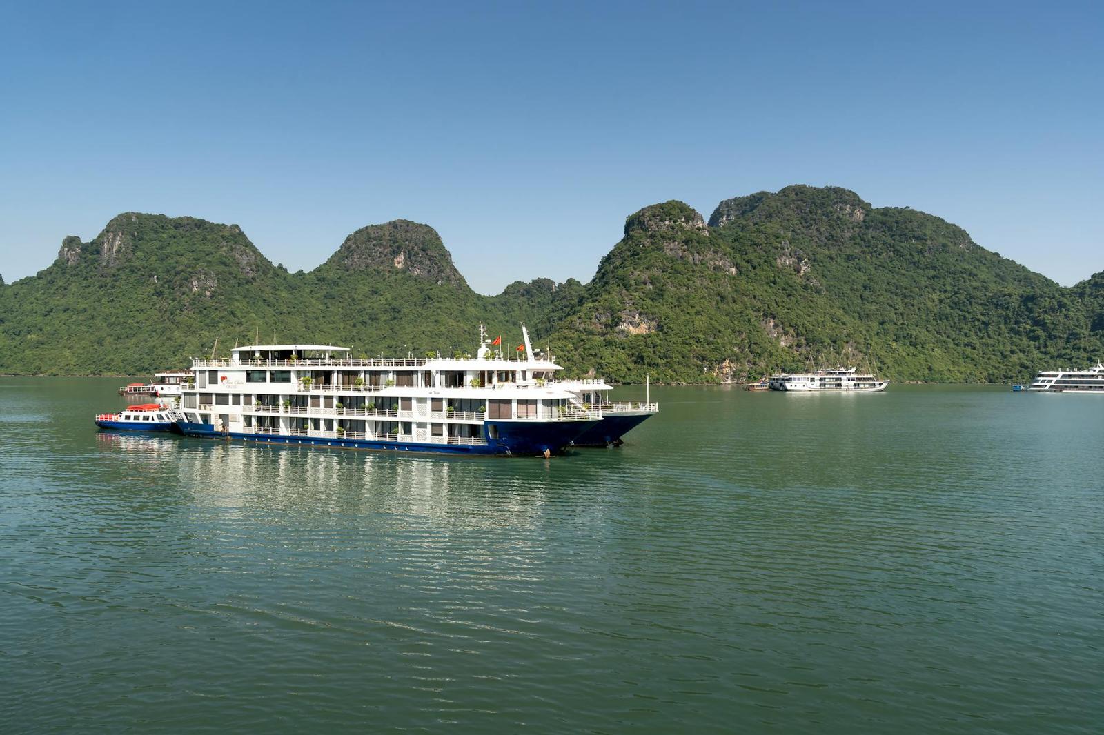 Cruise boat gliding past forested limestone peaks on a calm bay