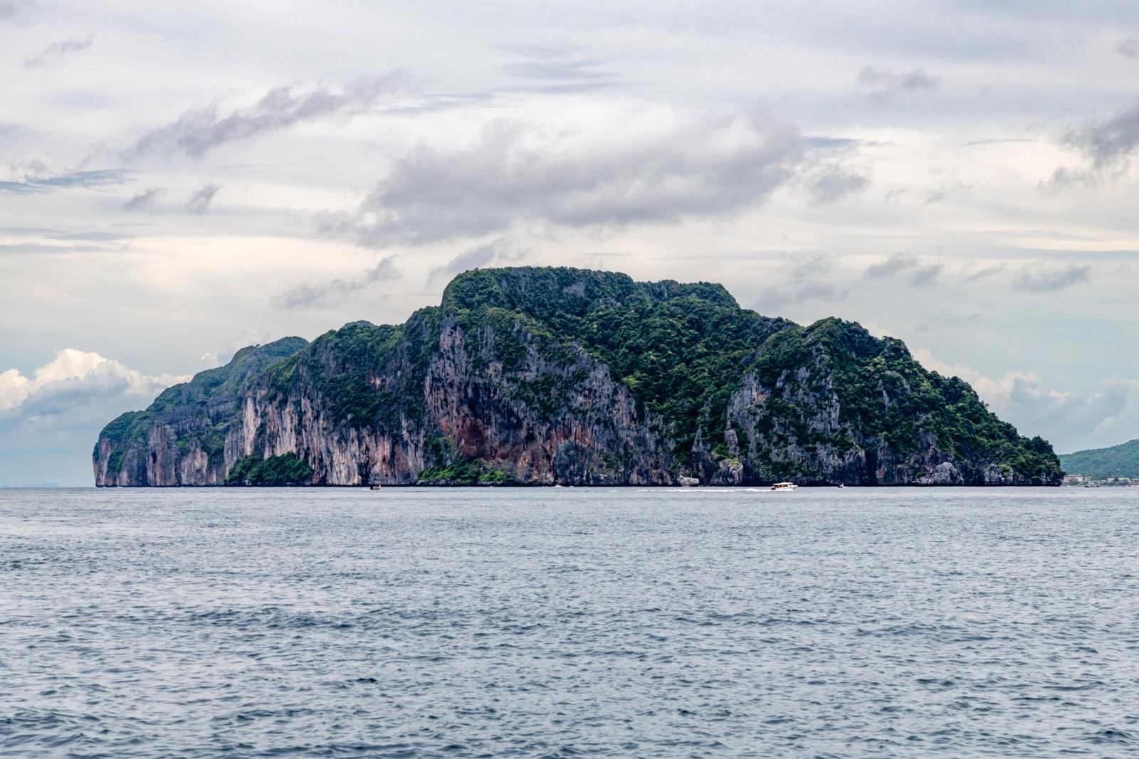 A breathtaking view of a rocky island cliff surrounded by the sea in Phuket, Thailand, under a cloudy sky