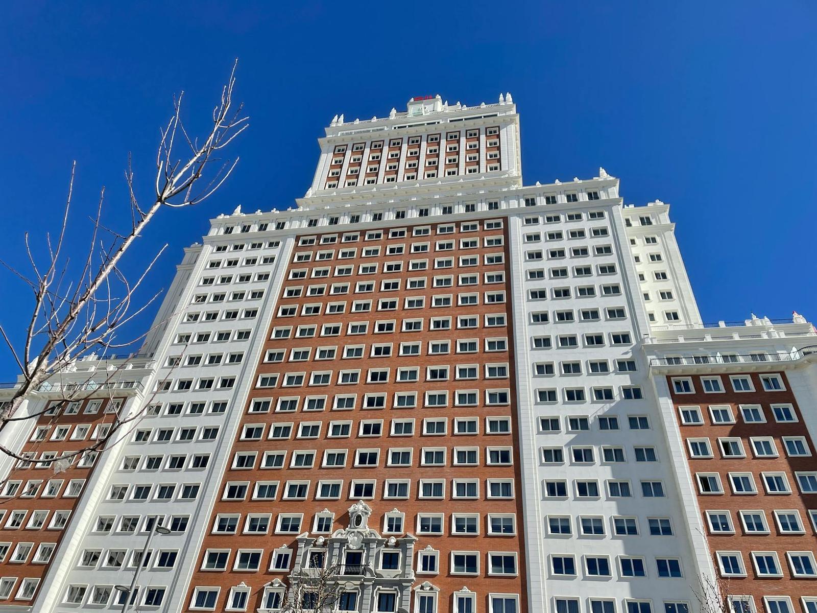 A tiered stone skyscraper facade rises steeply against a clear blue sky