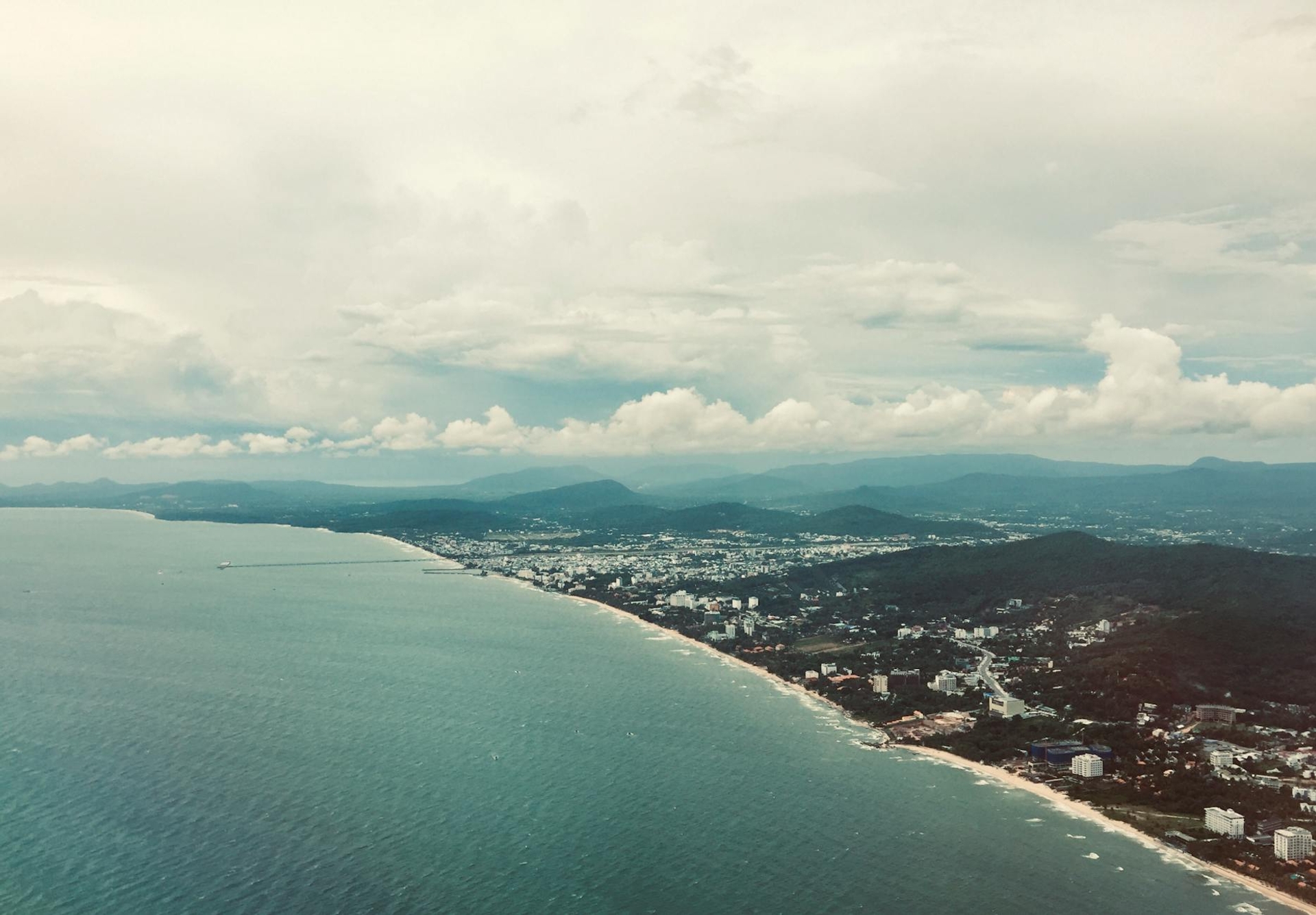 Aerial view of a coastal city stretching along the shoreline beneath hazy hills