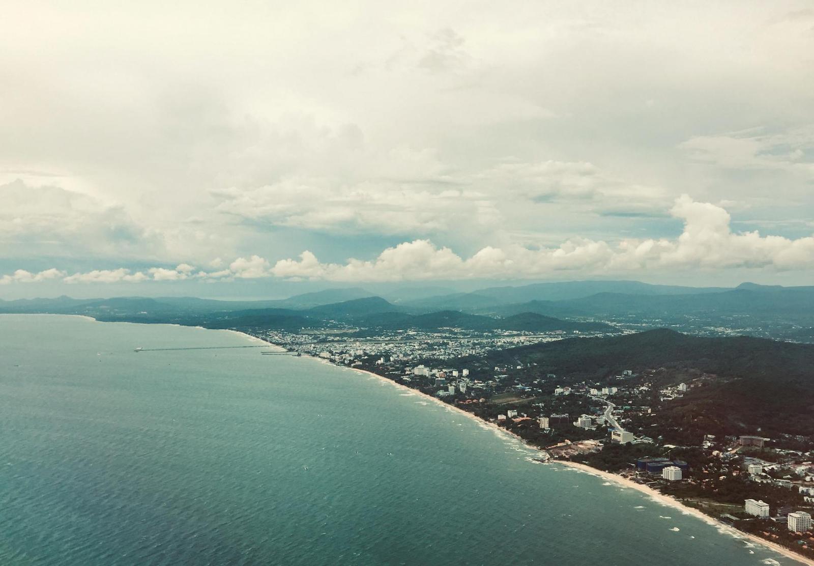 Aerial view of a coastal city stretching along the shoreline beneath hazy hills