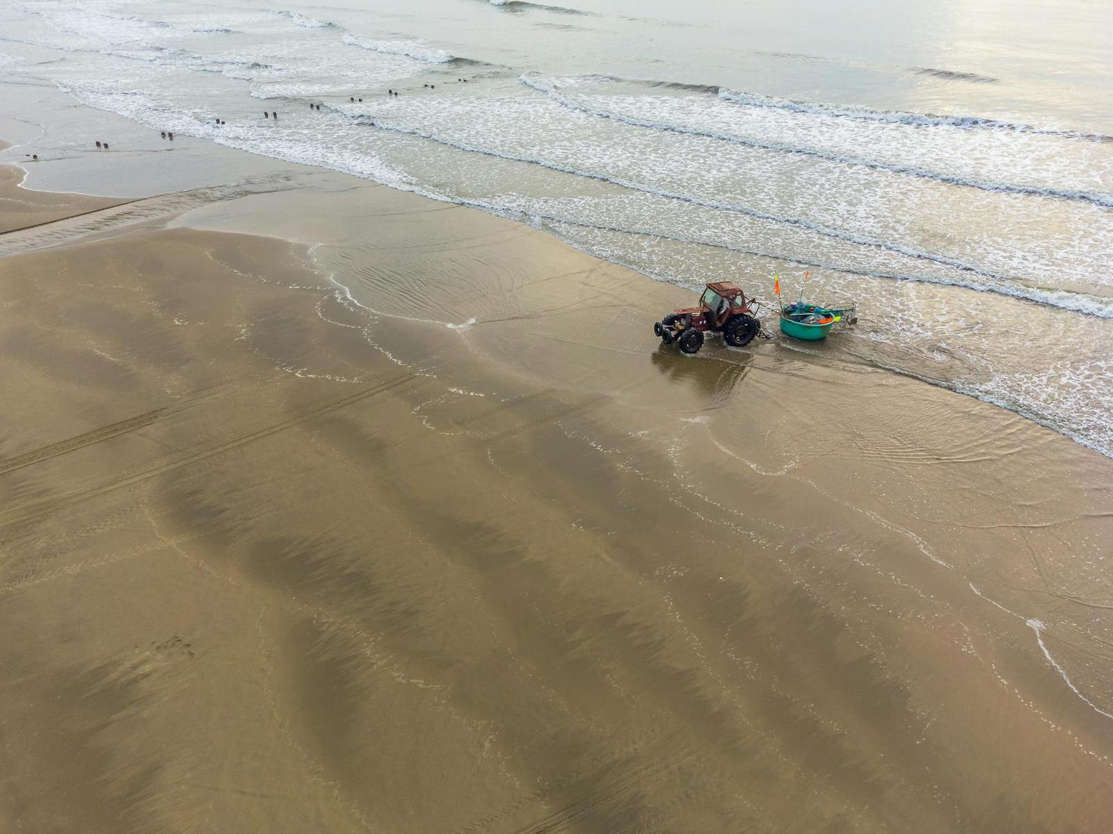 Aerial view of a tractor hauling a boat across a wide tidal beach