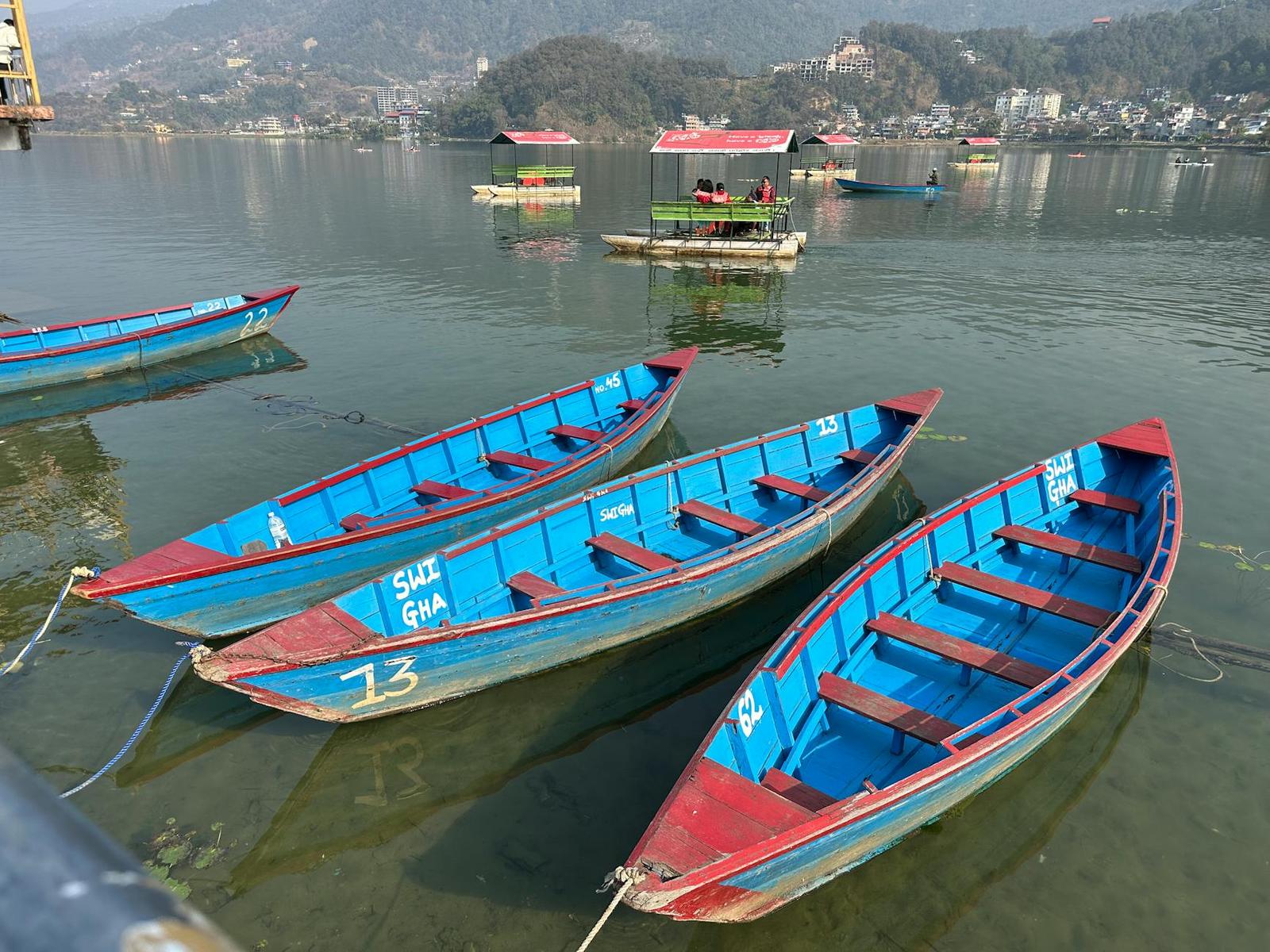 Vibrant wooden boats floating on Nepal's Phewa Lake with scenic mountain backdrop on a sunny day