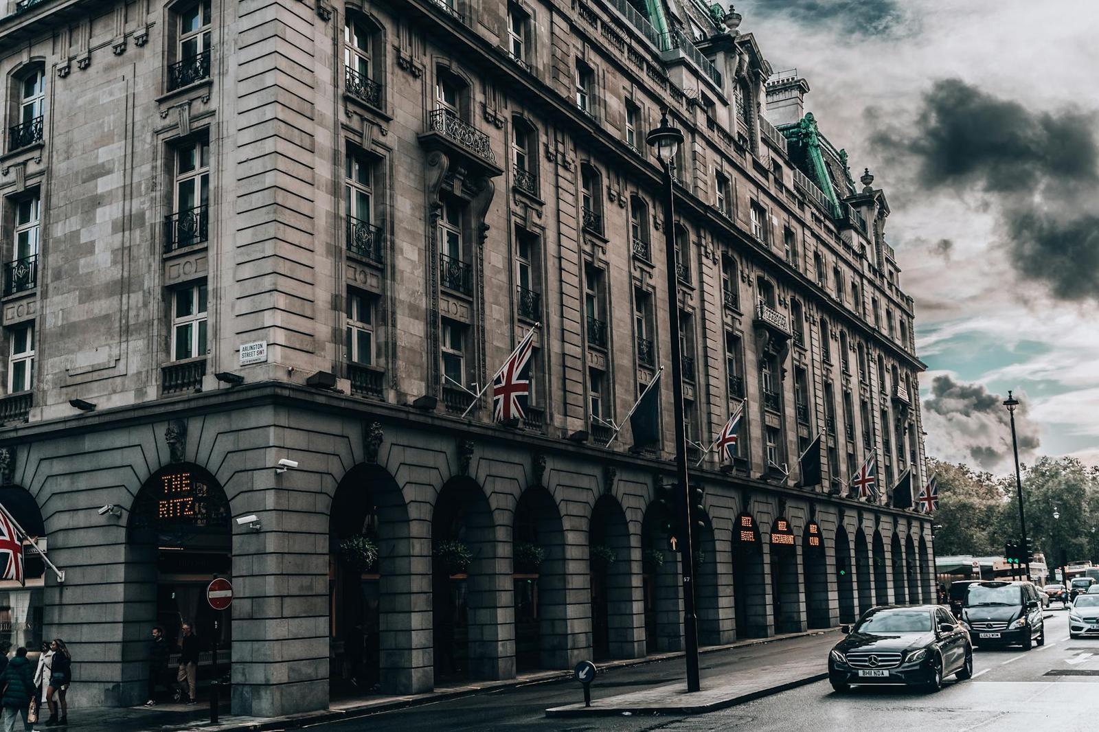 A grand stone hotel building on a street corner with national flags along its facade