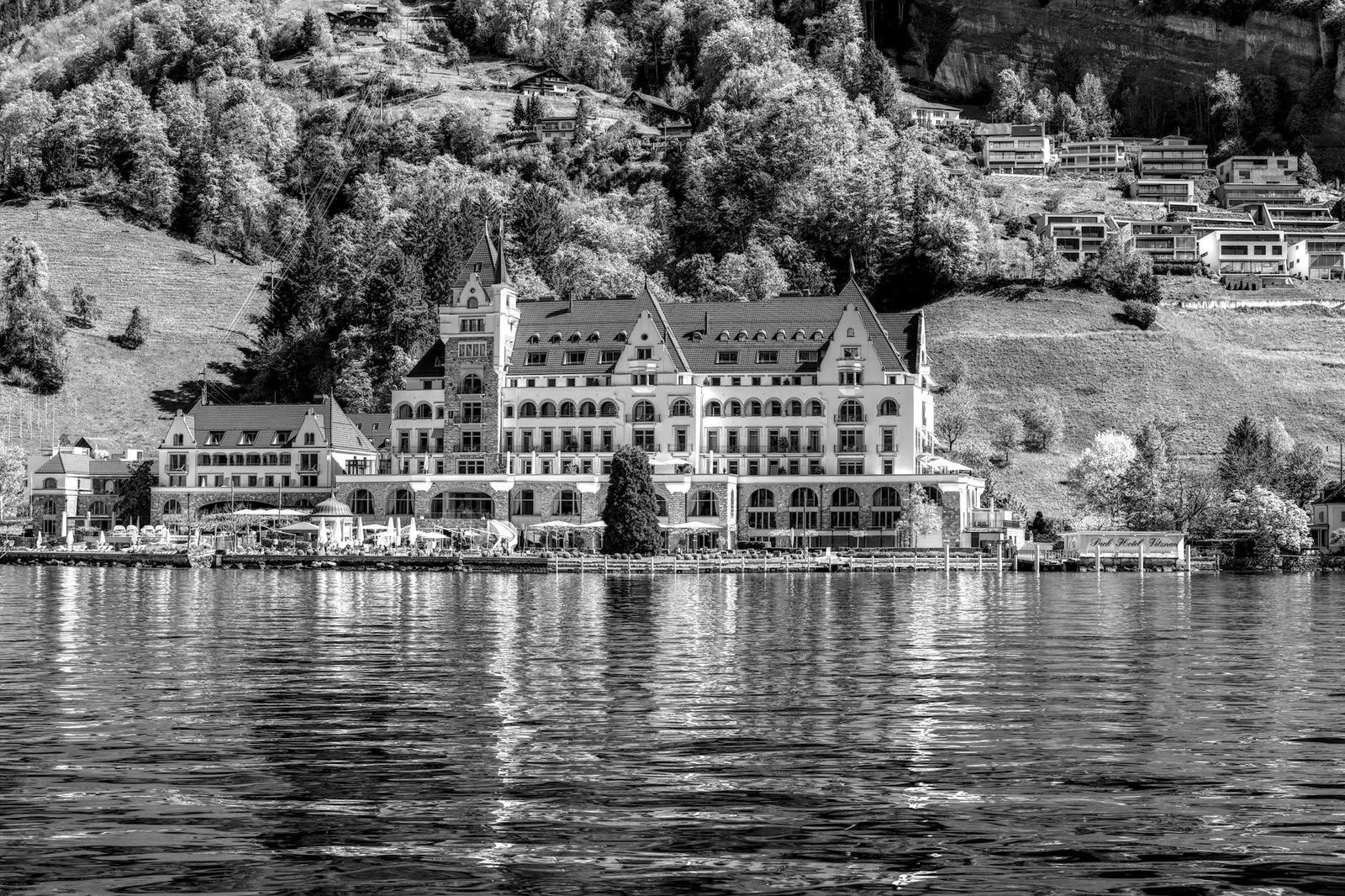 A grand turreted lakeside hotel building framed by wooded hills, in black and white