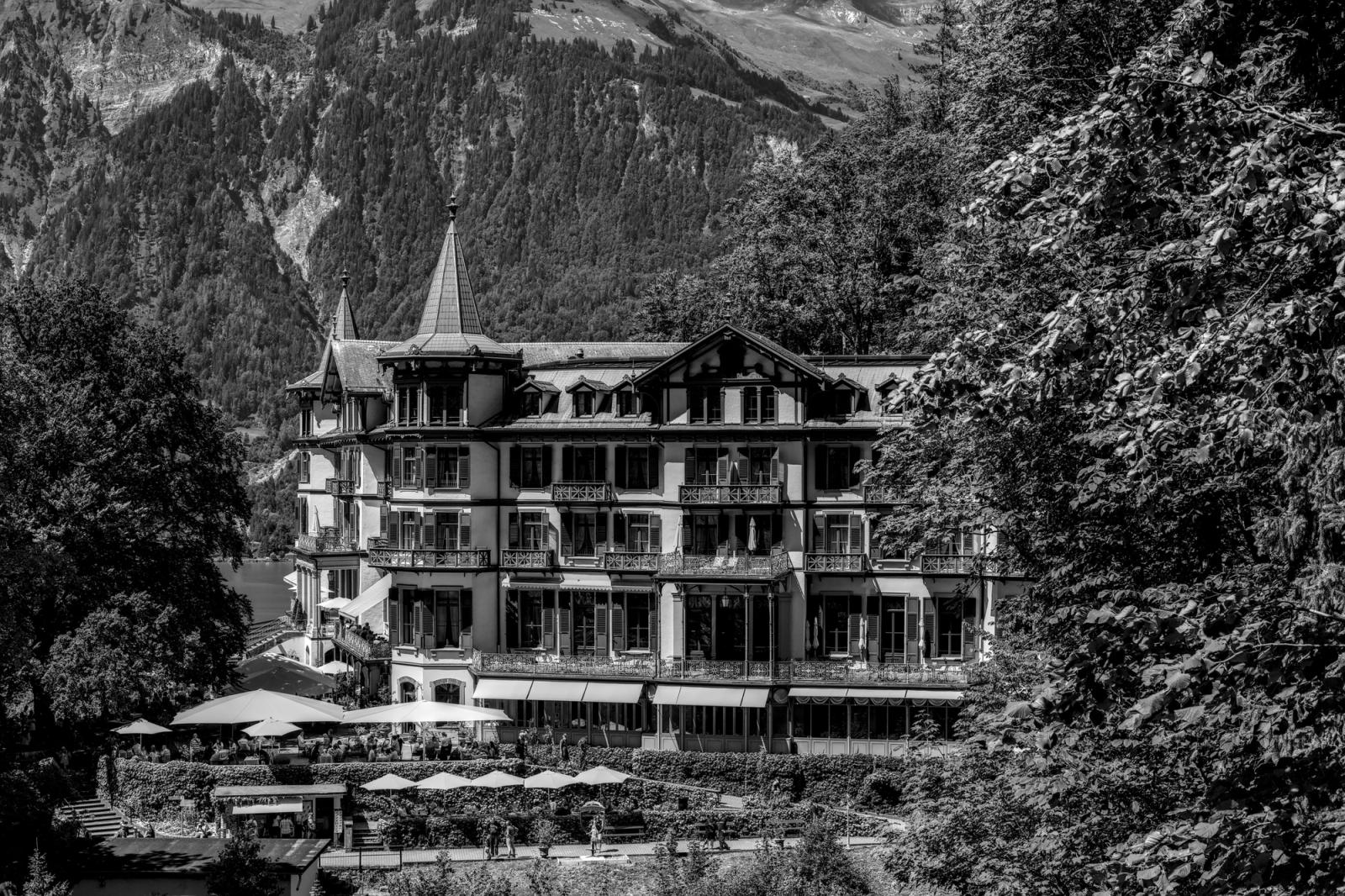 Black and white image of a historic Swiss hotel surrounded by mountains and trees