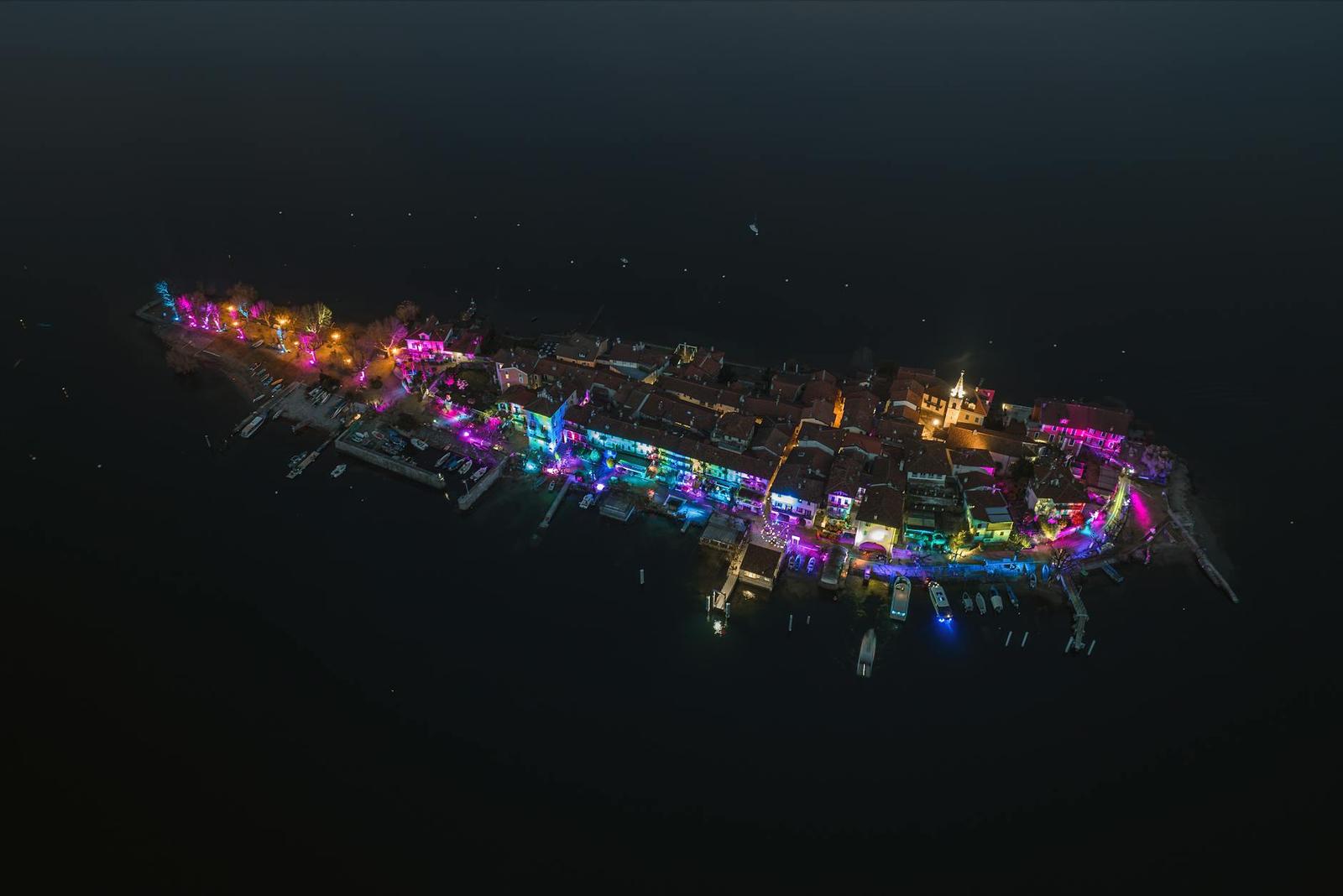 An aerial night view of a small island town glowing in colorful lights