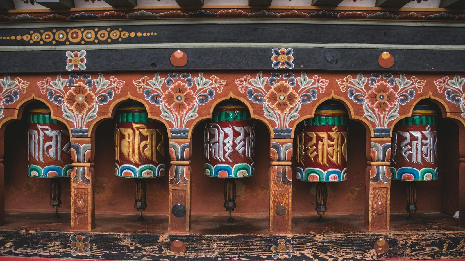 Row of painted wooden prayer wheels set into an ornately decorated temple wall