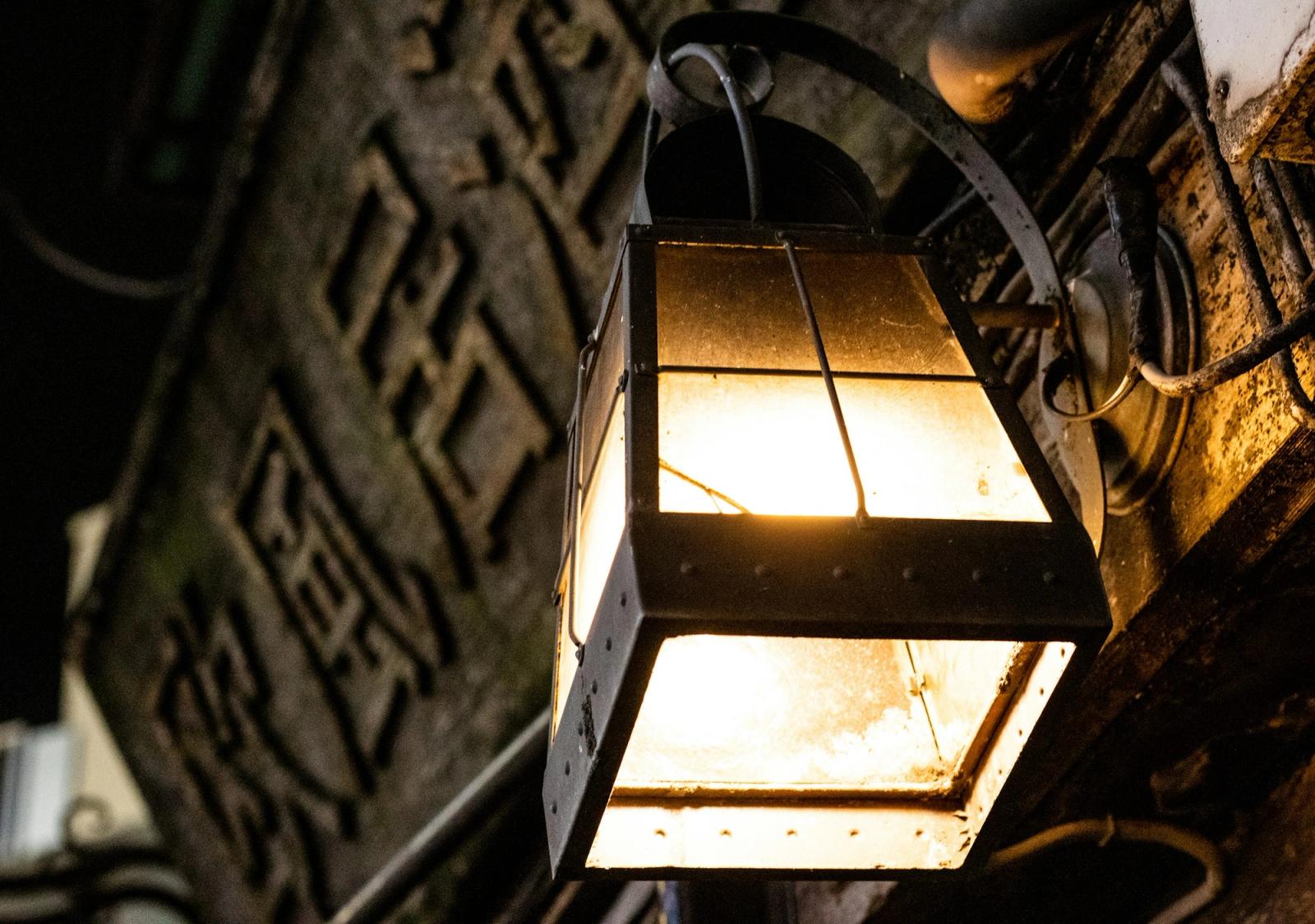 A lantern glowing against a weathered wall carved with Chinese characters