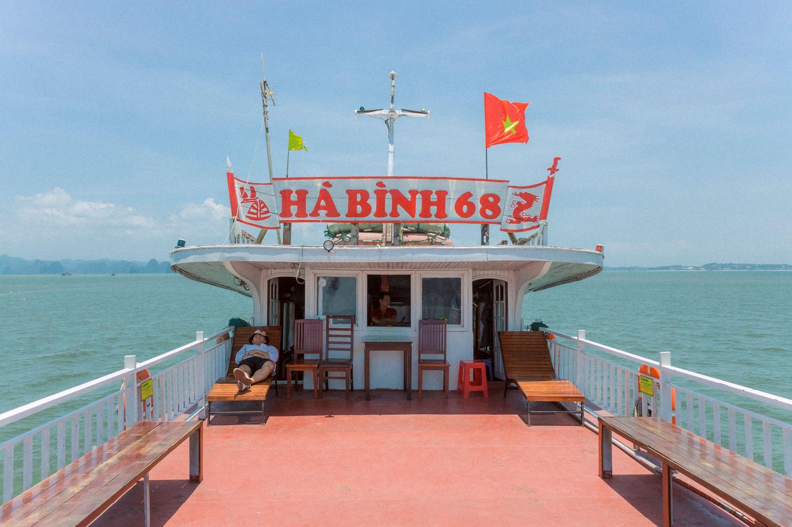 A man relaxes on a boat deck cruising through Halong Bay, Vietnam, under a clear blue sky